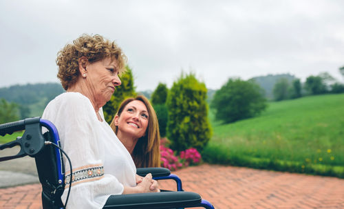 Senior woman sitting on wheelchair by granddaughter at park