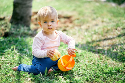 Full length of baby girl holding food sitting on grass outdoors