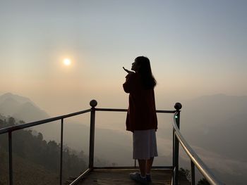 Rear view of person photographing on railing against sky during sunset