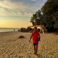 Portrait of man standing on beach against sky during sunset