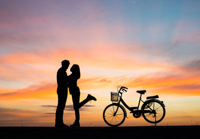 Silhouette man and woman standing against sky during sunset