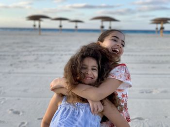 Portrait of smiling two young girls hugging  standing against sky near the beach. 
