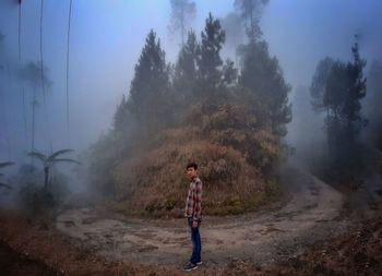 Man standing on street amidst trees against sky