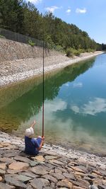 Man sitting by lake against trees