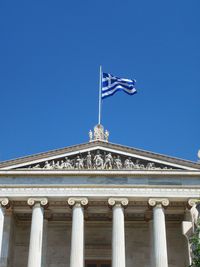 Low angle view of greek flag on historic building against clear blue sky