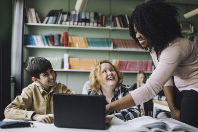 Smiling teacher helping students while doing e-learning in classroom