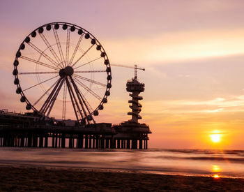 Ferris wheel at beach against sky during sunset