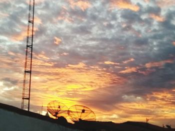 Silhouette electricity pylons against orange sky