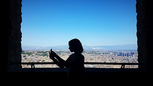 Silhouette woman looking at cityscape against clear sky