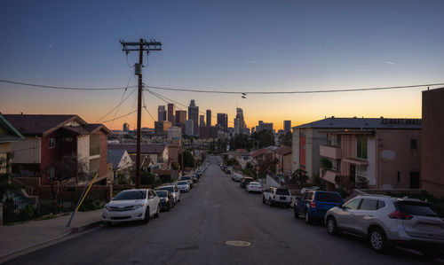 Cars on road by buildings against sky at dusk