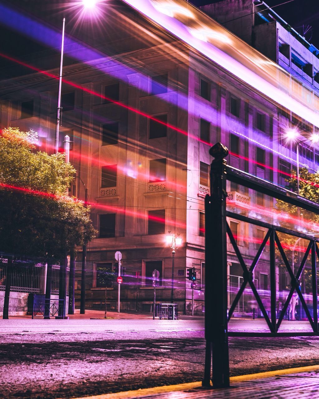 ILLUMINATED LIGHT TRAILS ON STREET AGAINST BUILDING AT NIGHT