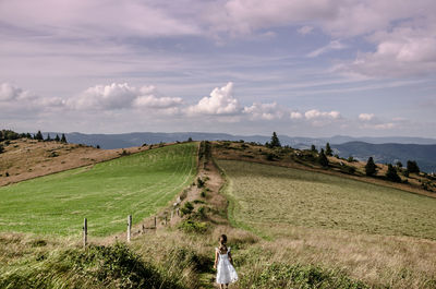 Rear view of girl walking on grassy mountain