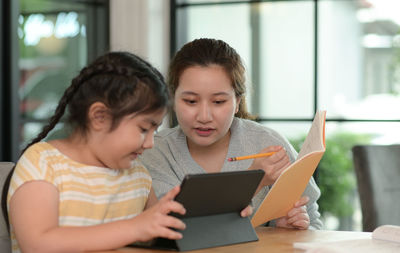 Asian girl studying privately with tutor at home, siblings teaching homework, online learning.