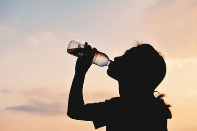 Silhouette woman drinking water from bottle against sky during sunset