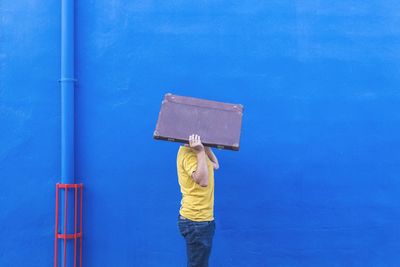 Side view of man carrying briefcase by blue wall