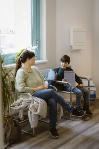 Mother and daughter sitting on chair in waiting room at clinic