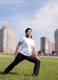 Portrait of man on grass in city against sky