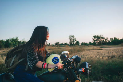 Rear view of woman sitting on motorcycle on field against sky during sunset