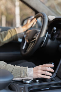 Girl holding one hand on steering wheel and another hand on gear shift lever. interior of vehicle.