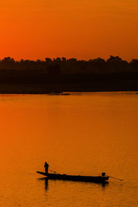 Silhouette person on lake against orange sky