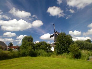 Wind turbines on grassy field against cloudy sky