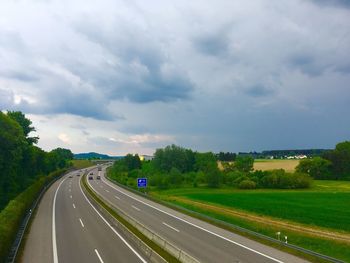 Road passing through landscape against cloudy sky