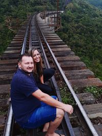 Portrait of smiling couple sitting on railroad track