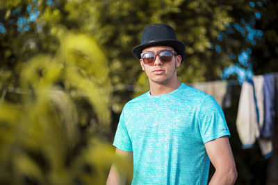 Portrait of young man wearing sunglasses standing against plants