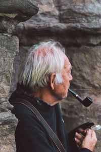 Mature man holding smoking pipe in mouth while standing outdoors