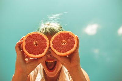 Low angle view of cheerful woman holding orange slices against blue sky