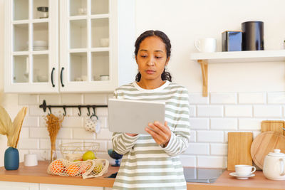 African-american female searching for recipe on tablet pc before cooking meal in kitchen