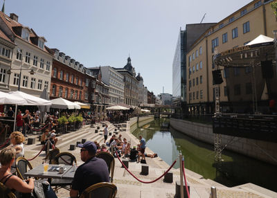 People on canal amidst buildings in city against sky