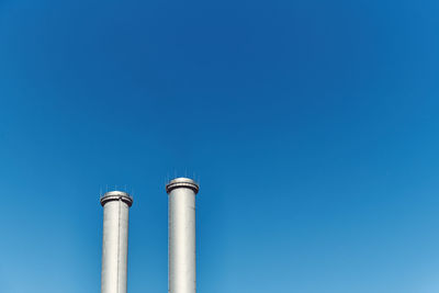 Low angle view of smoke stacks against blue sky