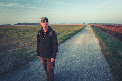 A man in sunglasses with a backpack goes the gravel road, autumn view