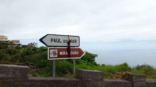 Information sign by sea against sky