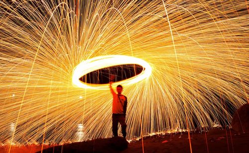 Full length of man standing against illuminated lighting equipment at night