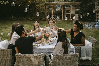 Smiling male and female friends toasting drinks while enjoying during social gathering