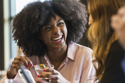 Cheerful businesswoman holding drink while looking at female colleague in hotel