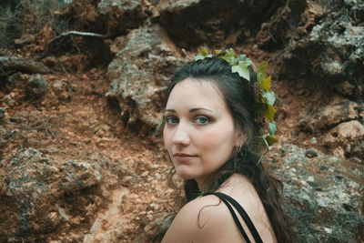 Portrait of young woman wearing leaf against rocks in forest