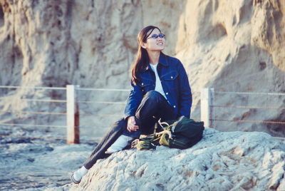 Full length of woman sitting on rock at beach