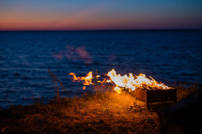 Bonfire by sea against sky during sunset