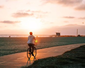 Rear view of man riding bicycle on road at sunset