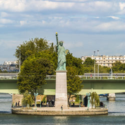 Statue of liberty by river against sky in city