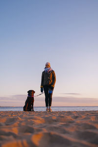 Rear view of woman walking at beach against sky during sunset