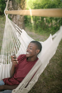 Smiling boy using mobile phone while relaxing on hammock in backyard