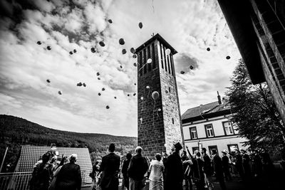 People releasing balloons by historic tower against cloudy sky