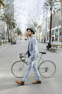 Male professional wearing hat while walking with bicycle in city