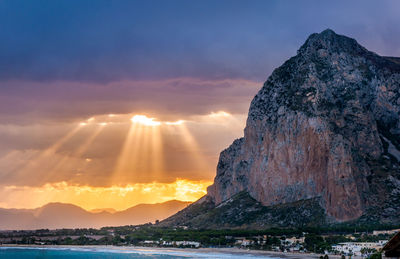 Low angle view of rocky cliff against cloudy sky during sunset