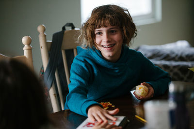 Girl with braces smiles at her sibling while holding an orange