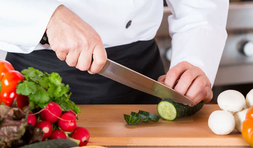 Midsection of chef cutting cucumber in commercial kitchen